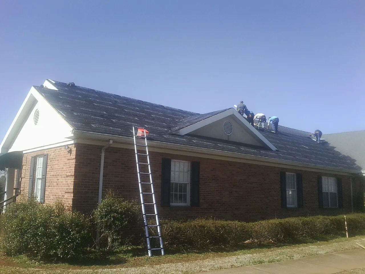 Crew tearing shingles off a brick ranch roof with a ladder set — Metal Roof Repair work by our crew in New Bloomington