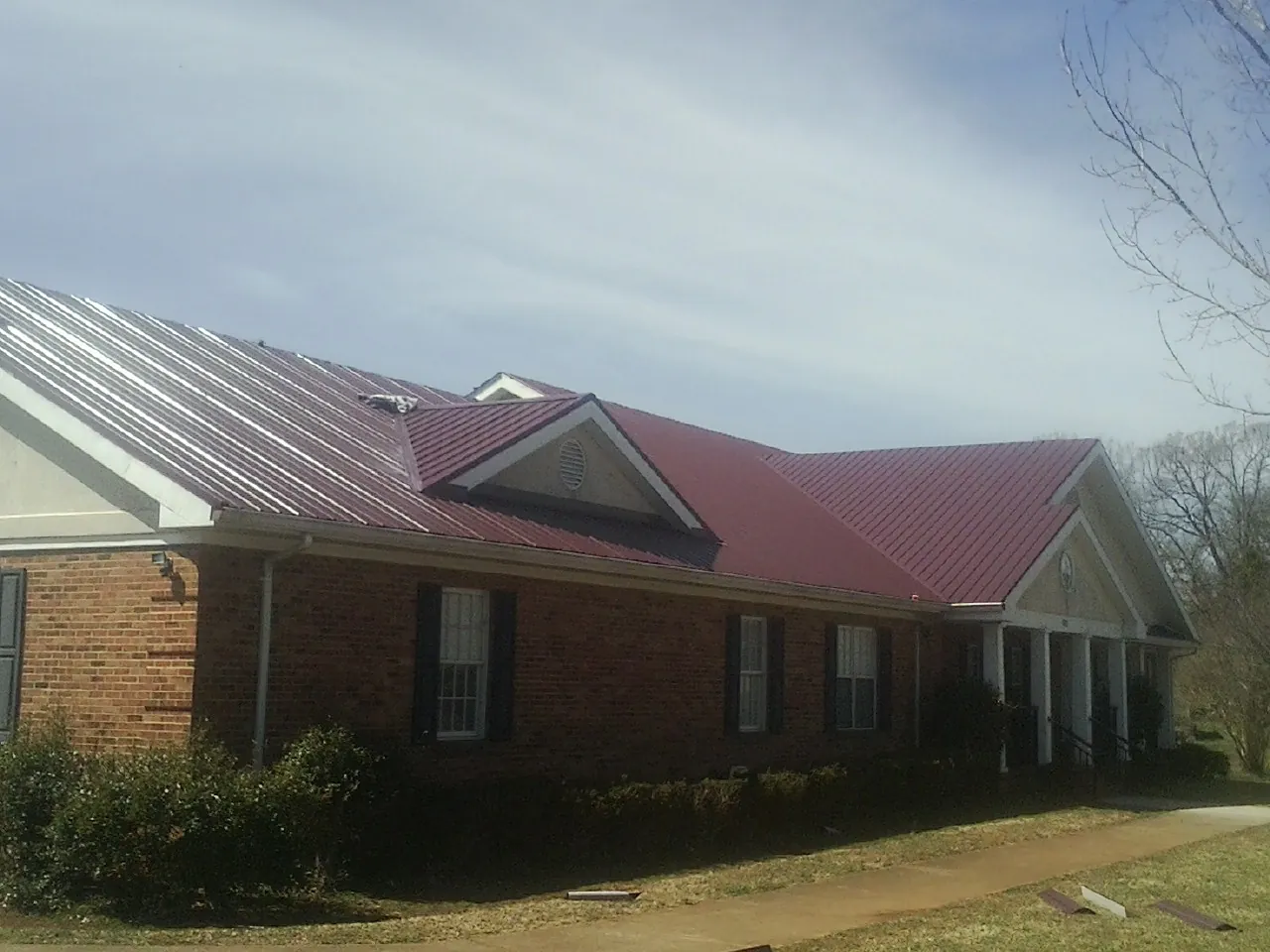 Red metal roof with gabled entries on a long brick building, from a Hail Damage Roof Repair job in New Bloomington