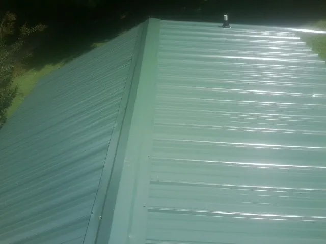 New green metal panels meeting at the ridge of a roof — Flat Roof Repair work by our crew in New Bloomington