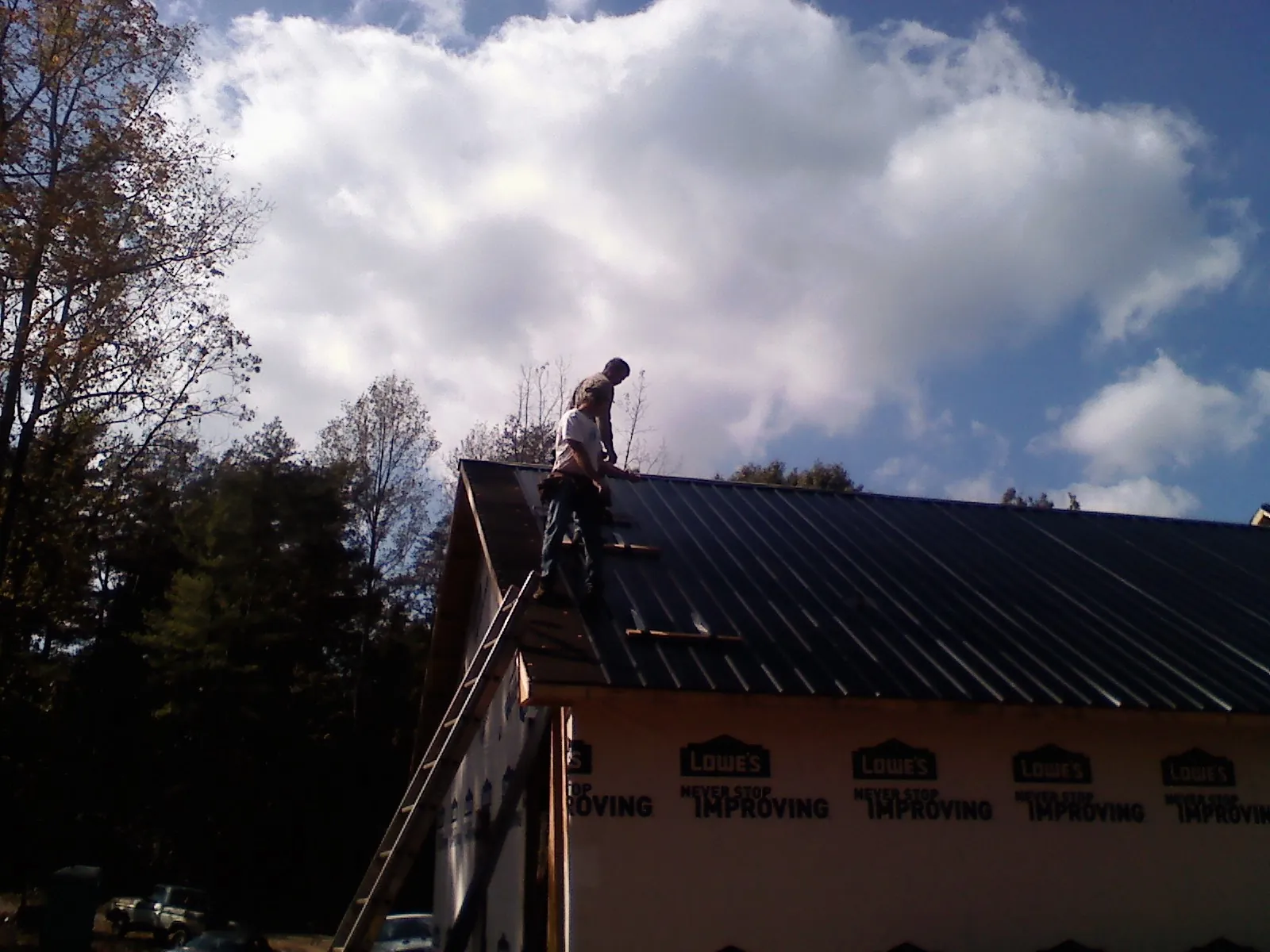 Roofer fastening dark metal panels high against a cloudy sky, from a Roof Inspection job in New Bloomington